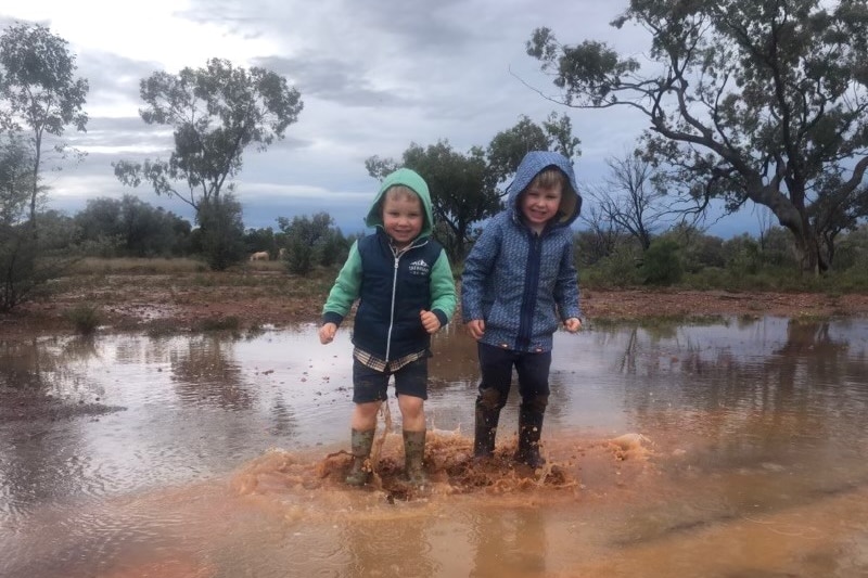Two young boys jump in a red mud puddle. 