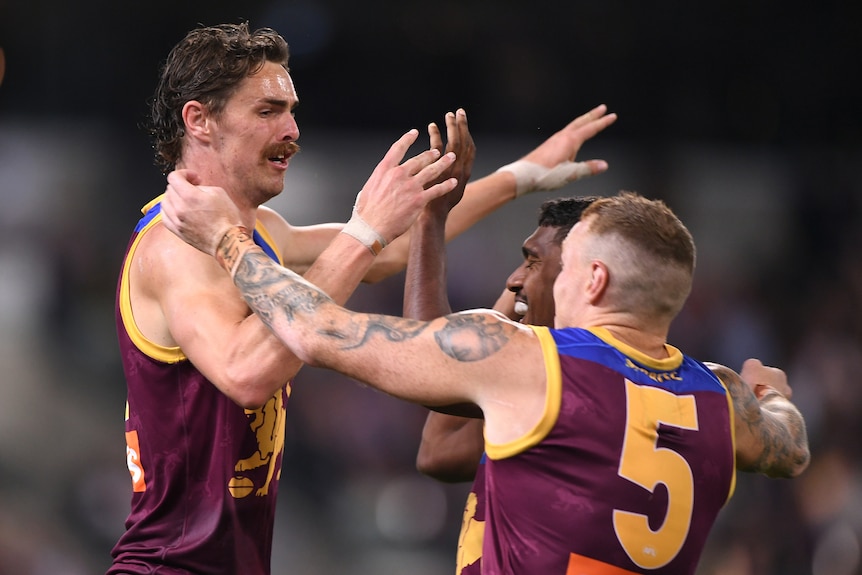 A Brisbane Lions AFL player receives high fives from two of his teammates.