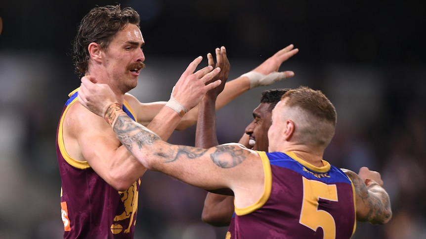 A Brisbane Lions AFL player receives high fives from two of his teammates.