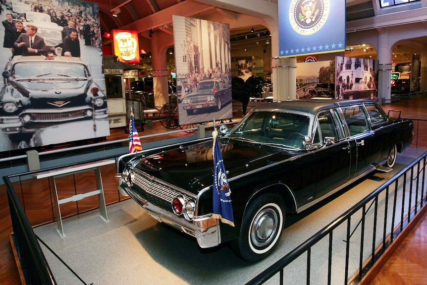 A black limousine lit and displayed on a platform inside a museum.
