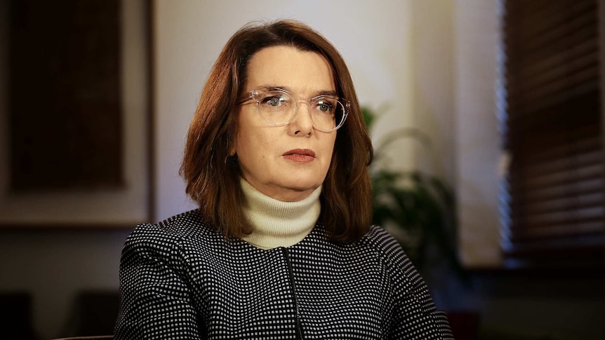 Portrait of woman sitting on white arm chair with shoulder length hair.