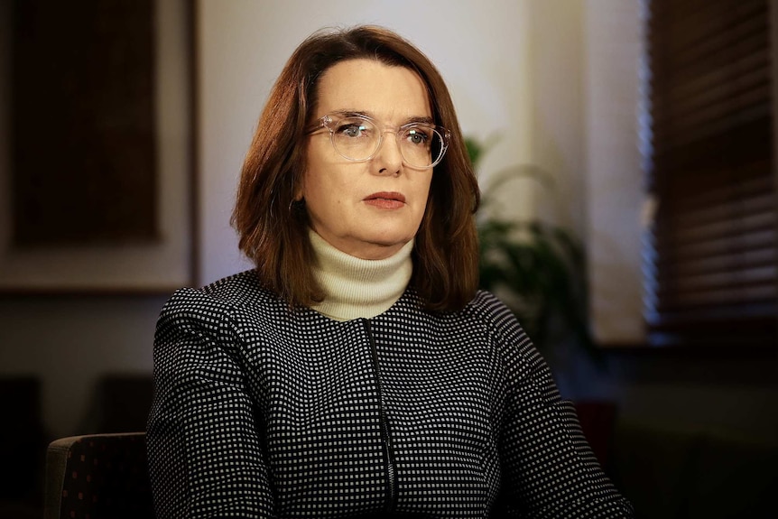 Portrait of woman sitting on white arm chair with shoulder length hair.