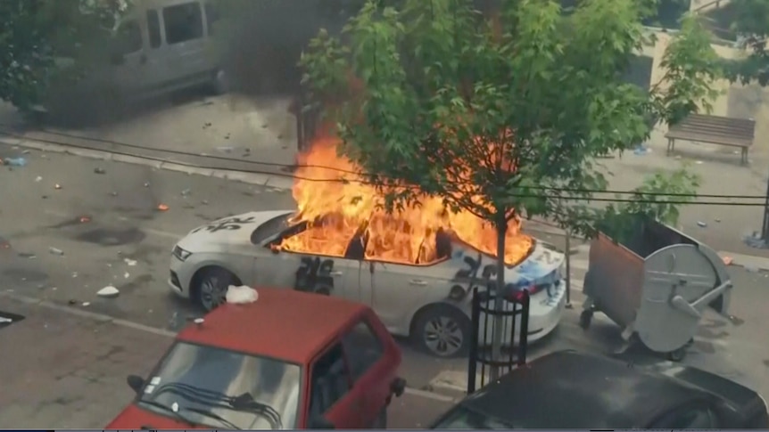 A Kosovar police car engulfed in flames with debris around it in the streets of Zvecan, Kosovo.