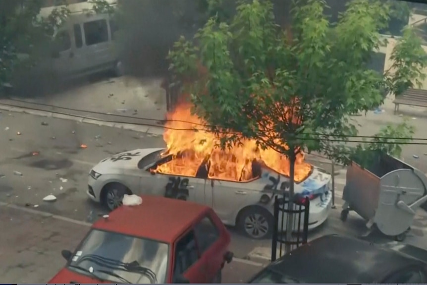 A Kosovar police car engulfed in flames with debris around it in the streets of Zvecan, Kosovo.