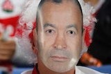 Two England fans sit in the stands wearing jerseys and red and white wigs. One is wearing a mask of Eddie Jones's face.