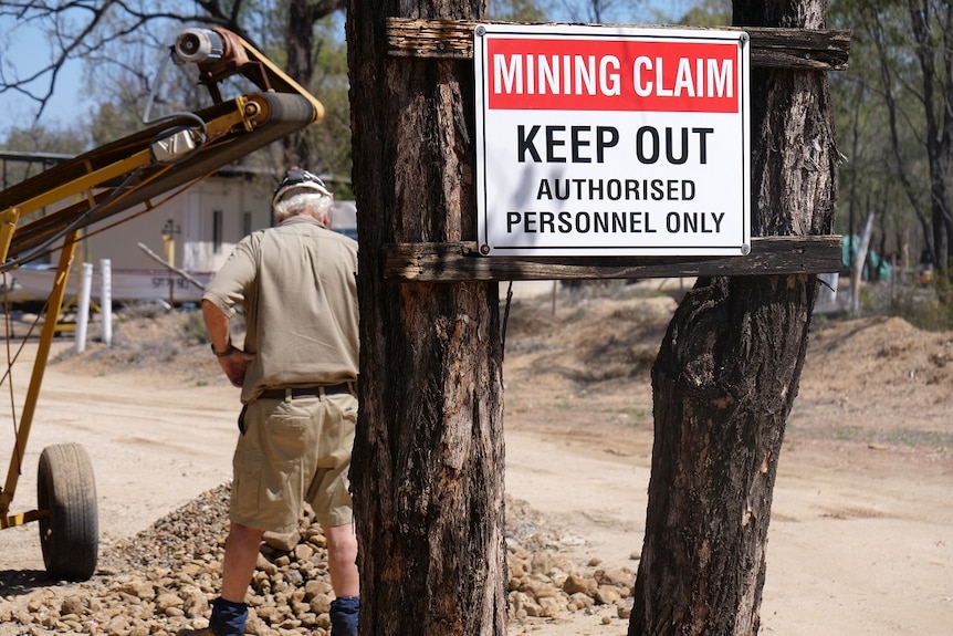mining claim, keep out, authorised personnel only, sign between trees, miner in background, conveyor belt behind.