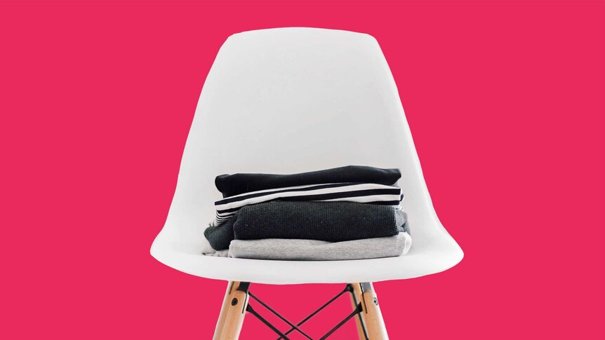 Black, white and grey clothes sit on a white chair to depict a capsule wardrobe.