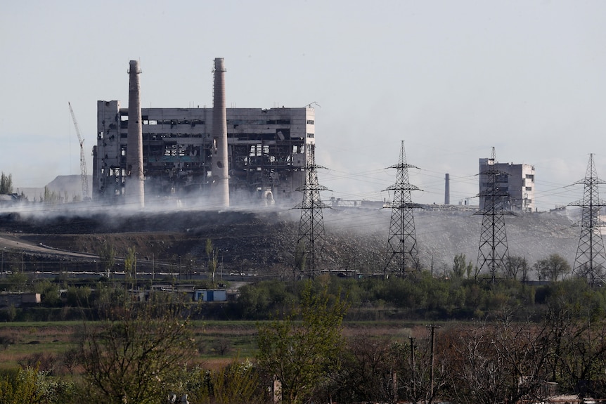 A large building surrounded by power lines is damaged with smoke lingering in the air.