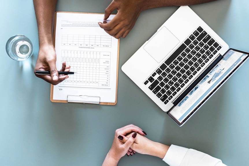 Photo of doctor writing on report and the patient's closed hands on the table showing giving a patient a bad diagnosis.