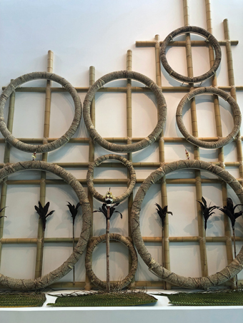 Series of cane rings mounted on a bamboo scaffold, against a white gallery wall.