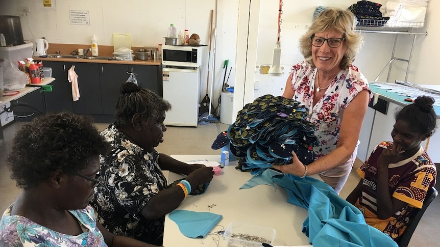 Moon Sick Car Bags founder Gay Muller holds a pile of washable sanitary pads while three Doomadgee women make more of them.