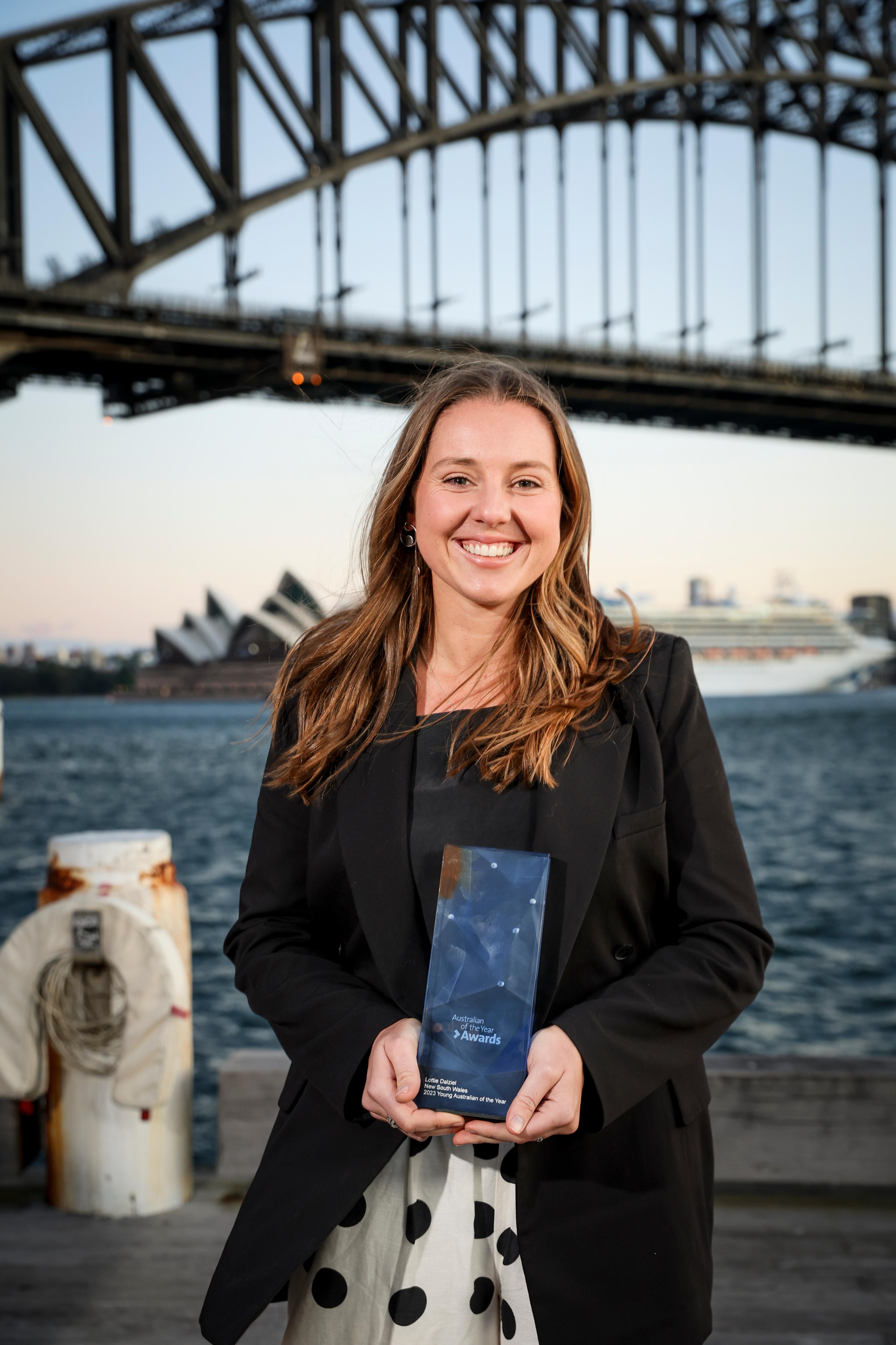 A young woman stands in front of sydney harbour holding a trophy