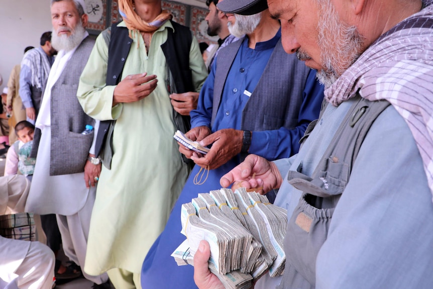 A group of men stand together holding a large bundle of bank notes.