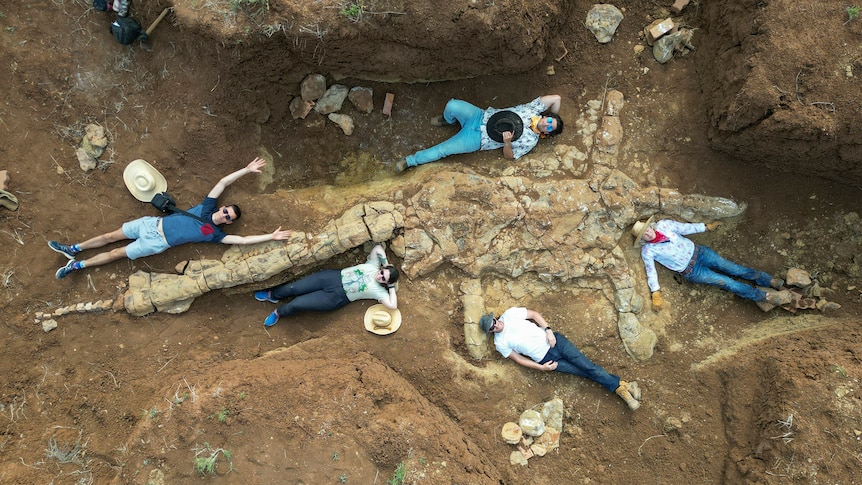 People lie on ground next to plesiosaur fossil