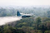 A C-130 Hercules aircraft dumps water over the canopy of the Amazon rainforest.