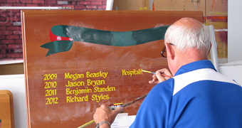 A white-haired man writing an honour board