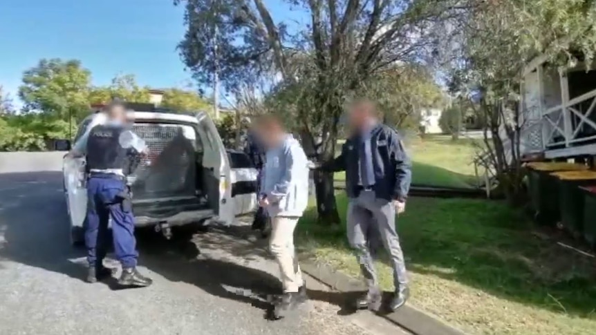 Police officers lead a man into the back of a police car