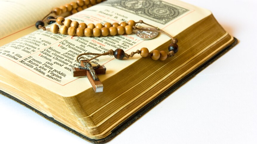 An open antique Catholic liturgy book with rosary beads and cross