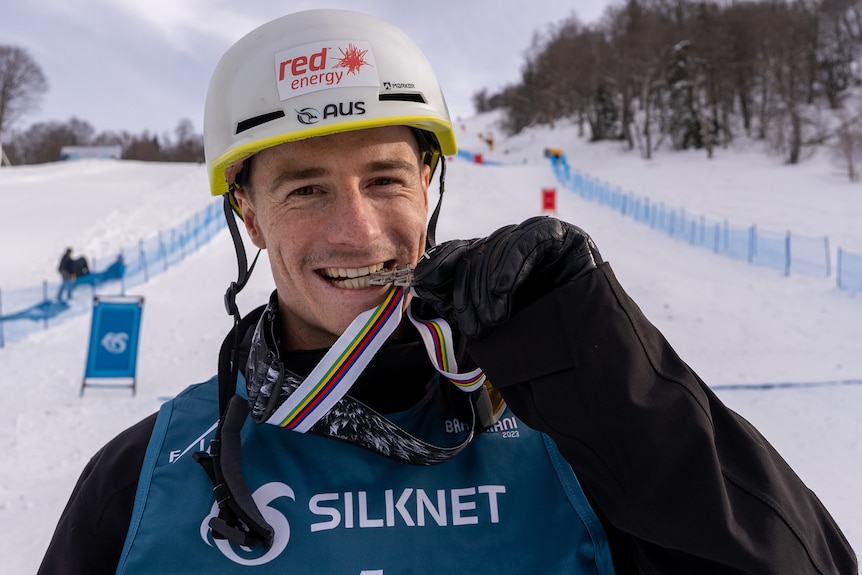 An Australian male moguls competitor bites into his silver medal as he celebrates at world championships.