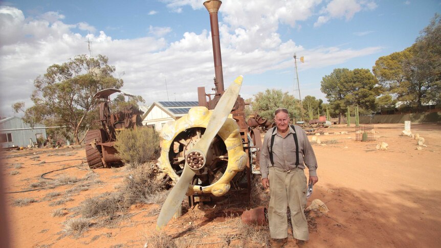 Doug standing with his favourite antique item, a old plane engine on the dry dirt of his homestead