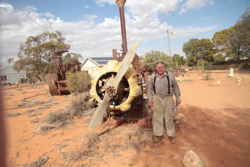 Doug standing with his favourite antique item, a old plane engine on the dry dirt of his homestead