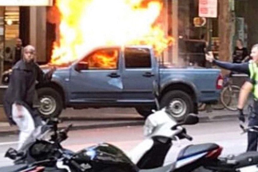 Suspect and police in front of car fire on Bourke Street