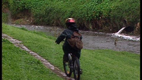 Child rides biycycle beside river on a rainy day