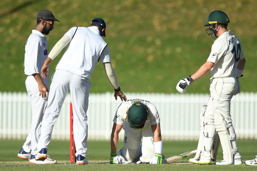A batsman is down on hands and knees after being hit by a ball, as cricketers check on him.