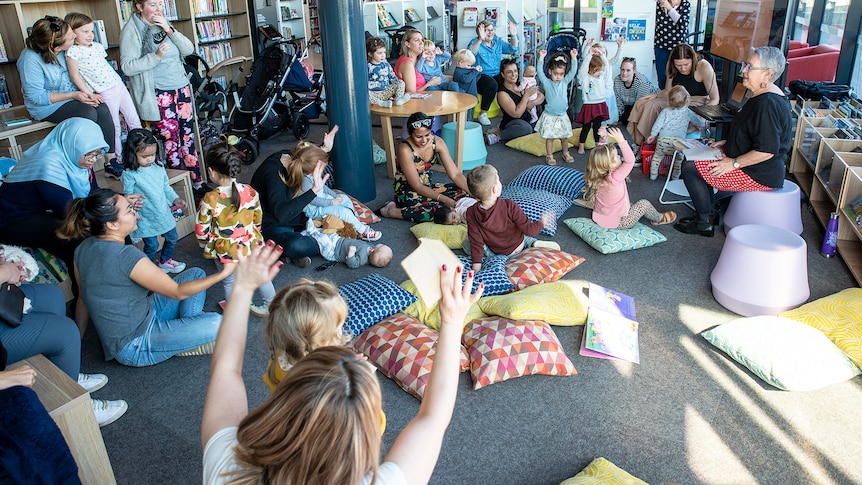 Children and adults sit around a woman reading a story 
