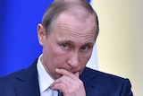 Vladimir Putin holds his hand to his face as he listens to someone asking a question.