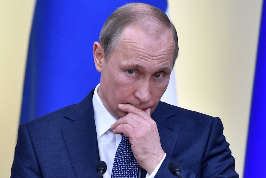 Vladimir Putin holds his hand to his face as he listens to someone asking a question.