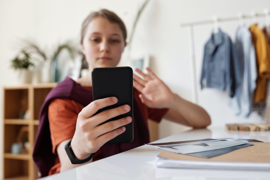 A young woman waves to someone on a video call on her phone.