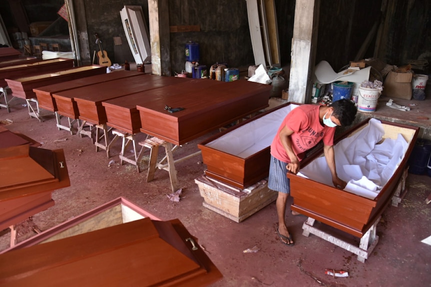 A worker wearing a protective face mask prepare coffins 