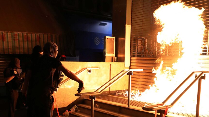 A large fireball erupts in front of a shuttered train station after a black-clad protester throws a petrol bomb.