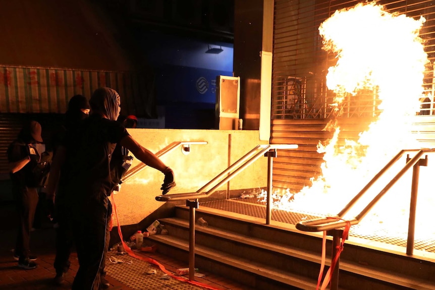 A large fireball erupts in front of a shuttered train station after a black-clad protester throws a petrol bomb.