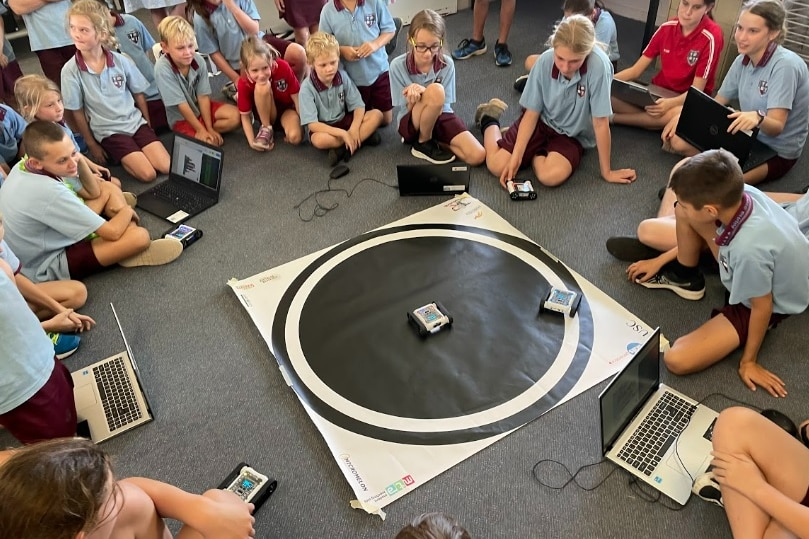 Kids in a classroom play with robotics equipment.