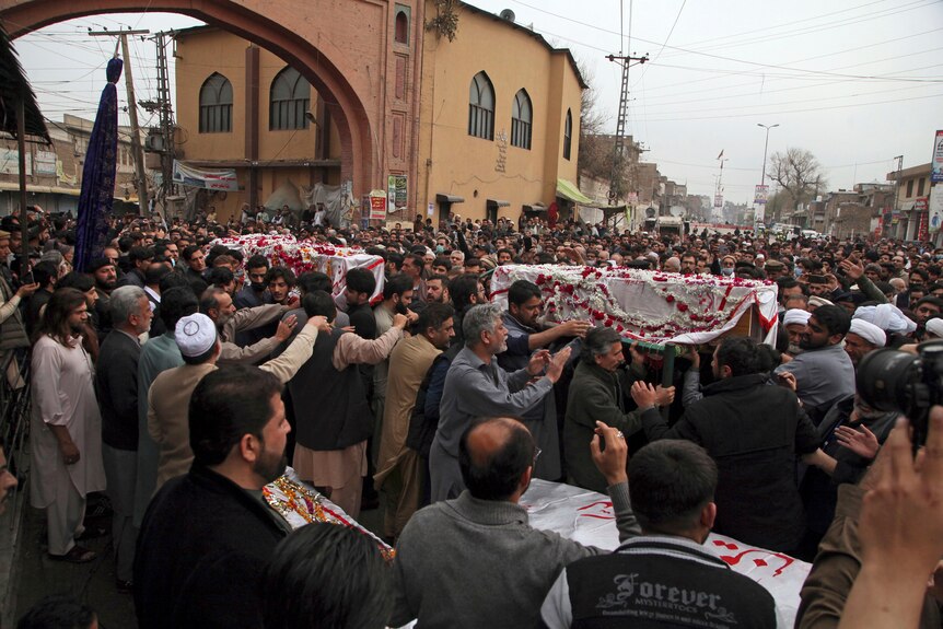 Hundreds of people are part of a funeral procession carrying coffins in the street.