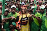 A woman in a yellow dress smiles at the centre of a large crowd dressed in green and waving flags