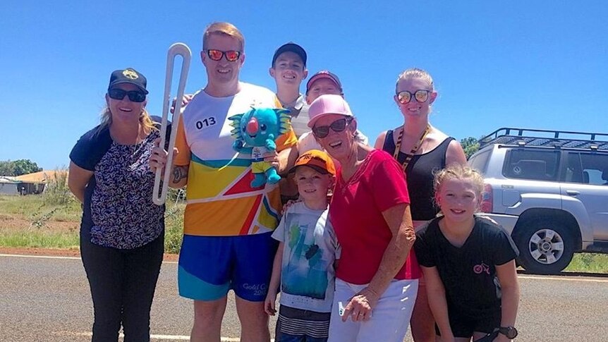 A man holding the Queen's Baton poses with his family in Karratha, WA