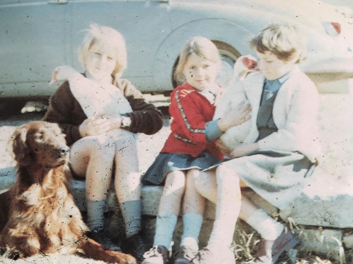 Three children under 10 sitting with geese and a dog on what looks like a footpath in the 1970s.