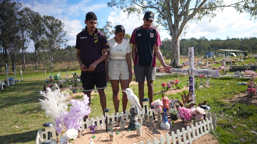 Michael, Rose and Orlyn stand, looking down at Constance Watcho's grave.