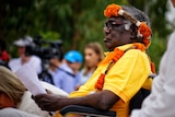 Galarrwuy Yunupingu sits in a wheelchair wearing a yellow shirt and traditional headdress.