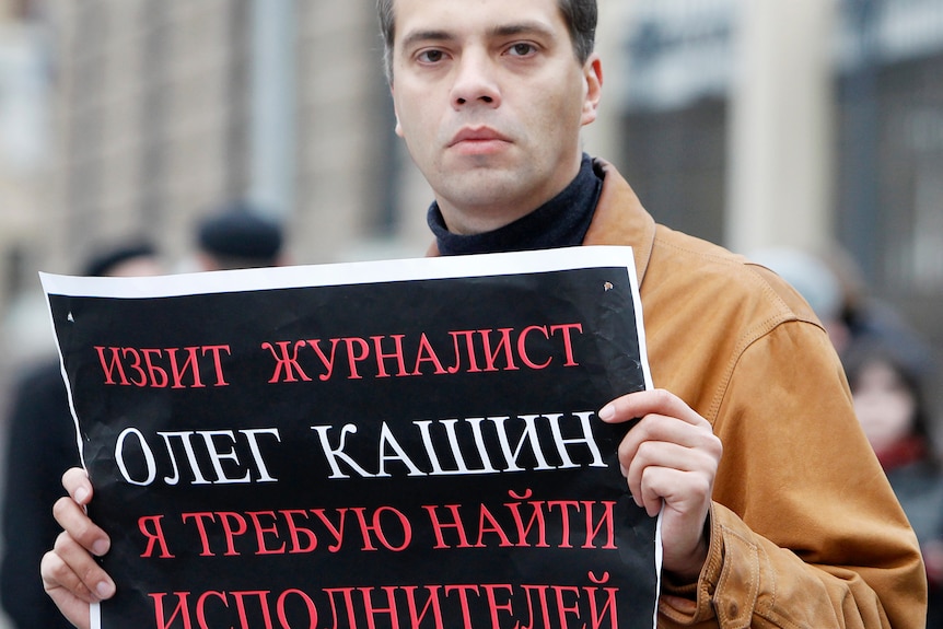 Milov, in a brown jacket, holds up a sign in Russian.