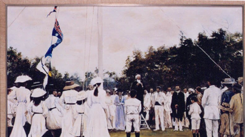 A photo painted in the early 1900s shows a group of men and women standing around a flag pole.