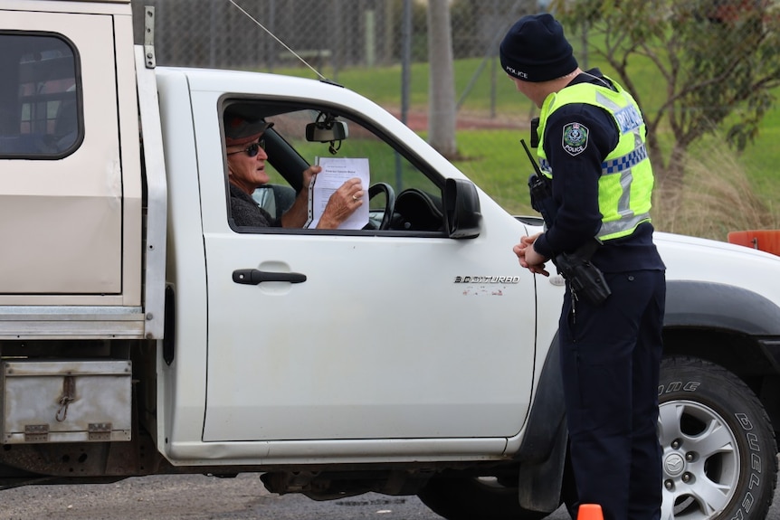 A man in a police uniform stands next to a man driving a ute