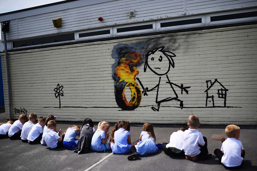 Children sit on ground in front of mural