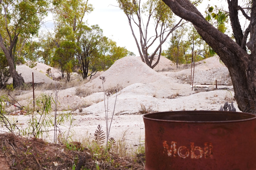 Old mobil rusted fuel can in foreground, white piles of rocks in the background with trees.