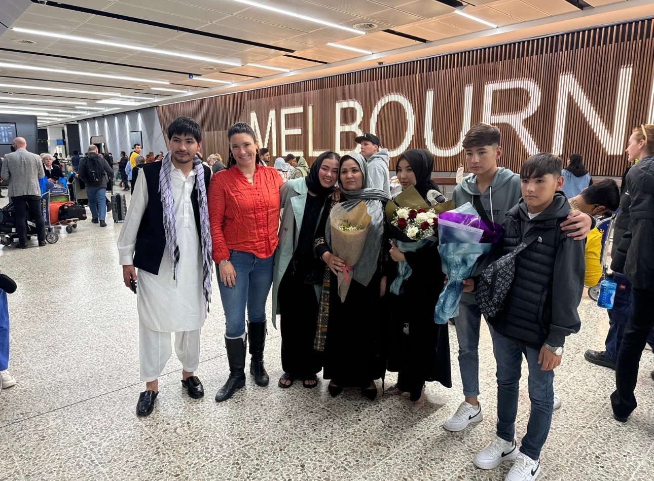 A family stand in front of the arrivals hall at Melbourne airport, smiling at the camera