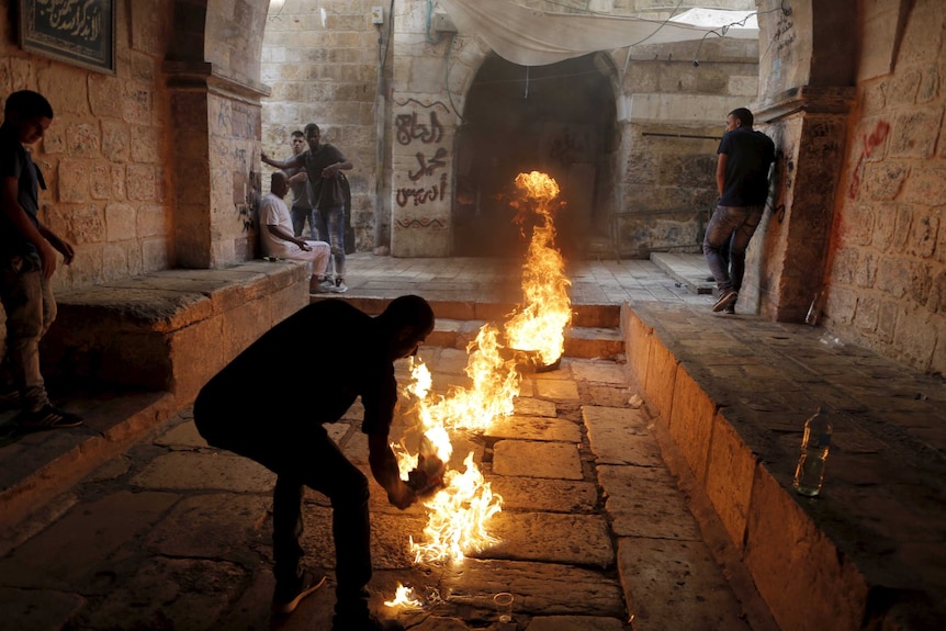 A Palestinian protester kicks a burning tyre