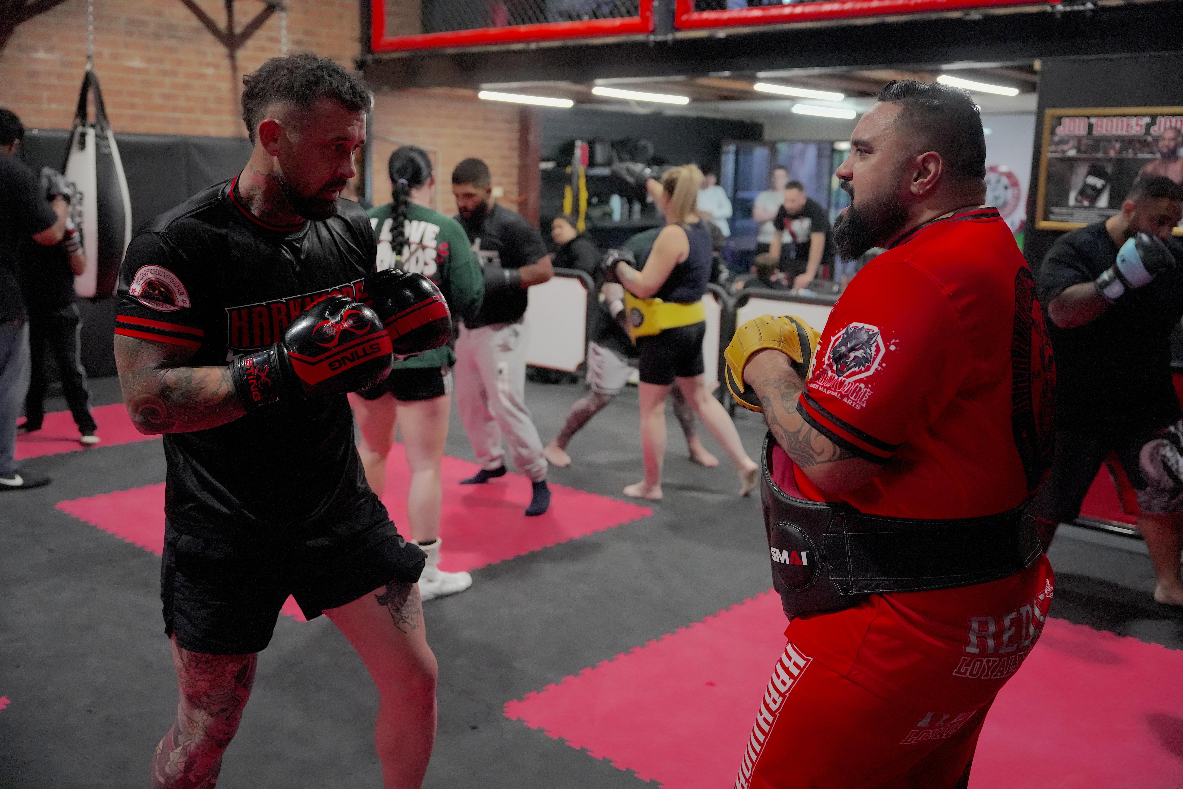 Two men train wearing boxing gloves in a gym.